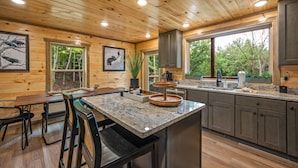 L’intérieur d’une cabane en bois comprend un coin cuisine doté d’un comptoir en granit, de meubles de rangement en bois et d’une table à manger avec des chaises.