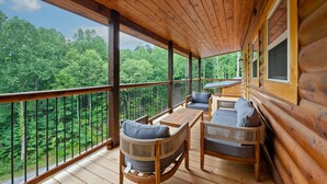 Une terrasse en bois, dotée de mobilier d’extérieur et offrant une vue sur une forêt.