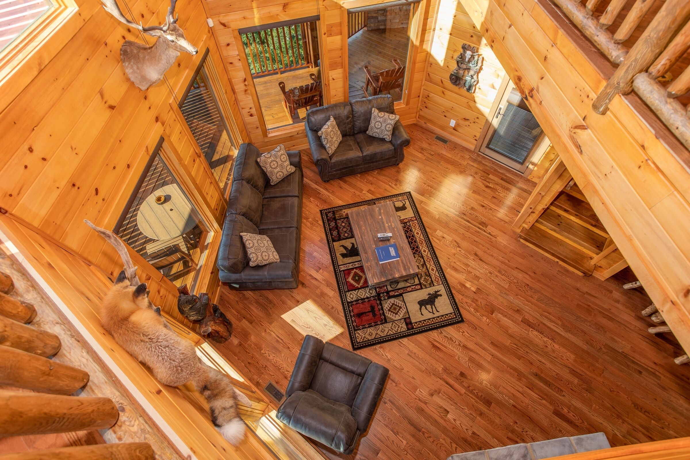 A log cabin interior with a wooden floor, a sofa set, a coffee table, and a deer head mounted on the wall.
