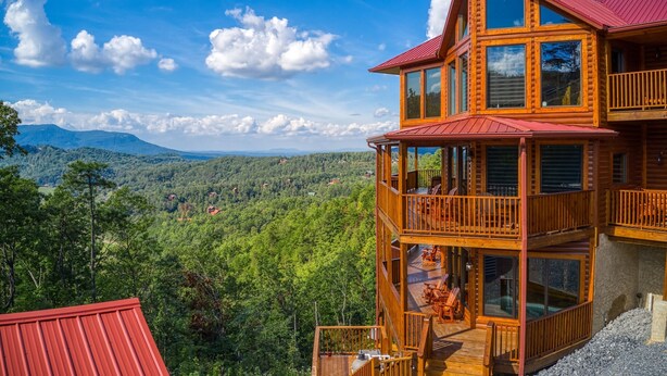 A multi-level wooden cabin with balconies, set against a backdrop of a mountainous landscape. - Luxurious 5-Bedroom Cabin with Indoor Pool (SEVIERVILLE)