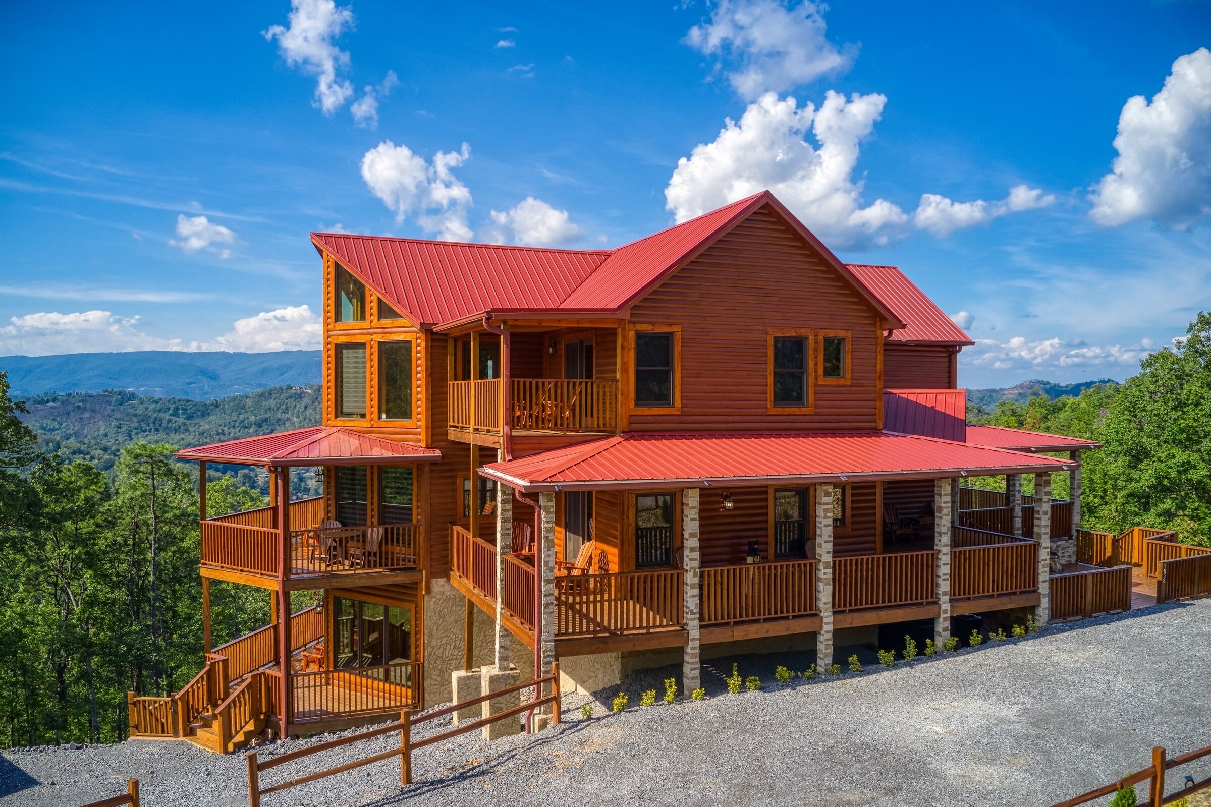 A two-story wooden cabin with a red roof, multiple balconies, and a gravel driveway.