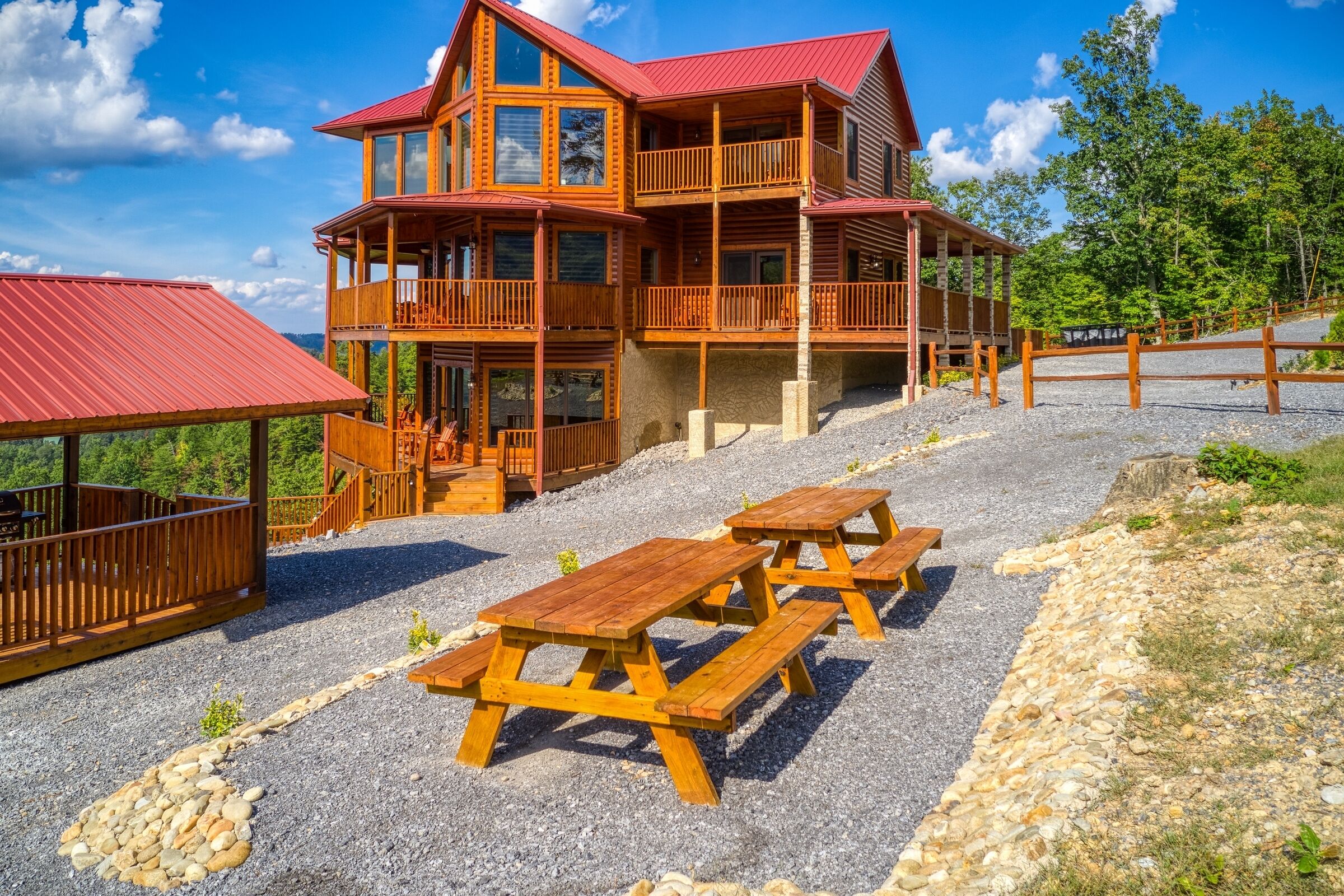 A multi-story wooden lodge with balconies, picnic tables, and a gravel driveway.