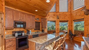 A wooden cabin kitchen with granite countertops, a built-in oven, and a stone island. - Luxurious 5-Bedroom Cabin with Indoor Pool (SEVIERVILLE)