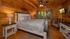 A wooden cabin bedroom with a bed, nightstand, dresser, and a ceiling fan. - Cozy Den Cabin with Covered Porch and Games (PIGEON FORGE)