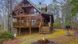 A log cabin with a balcony, a fire pit, and a stone wall foundation. - Cozy Den Cabin with Covered Porch and Games (PIGEON FORGE)