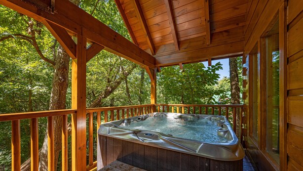 A wooden deck with a hot tub and a bench. - Cozy Den Cabin with Covered Porch and Games (PIGEON FORGE)