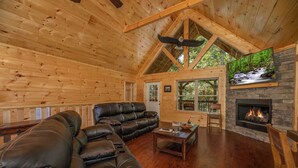 A log cabin interior with a large leather sofa, a fireplace, and a television mounted on the wall. - Modern Cabin with Fireplace and Game Room (PIGEON FORGE)