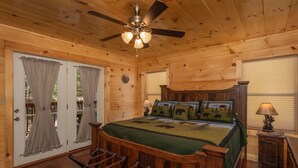 A wooden cabin bedroom with a bed, a ceiling fan, and a small table with a lamp. - Modern Cabin with Fireplace and Game Room (PIGEON FORGE)