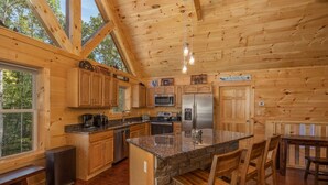 A wooden cabin kitchen with granite countertops, a central island, and a dining area. - Modern Cabin with Fireplace and Game Room (PIGEON FORGE)