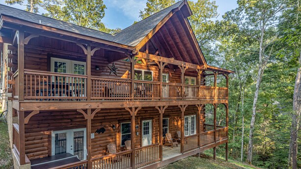 A two-story log cabin with a balcony and a porch, surrounded by trees. - Modern Cabin with Fireplace and Game Room (PIGEON FORGE)