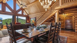 Une salle à manger spacieuse avec un plafond haut, des poutres en bois et un escalier menant à un niveau supérieur.