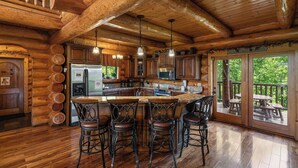 L’intérieur d’une cabane en rondins comprend une grande cuisine, des tabourets de bar en bois et un espace extérieur aménagé en terrasse.