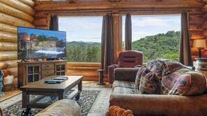 L’intérieur d’une cabane en rondins, avec un téléviseur diffusant une image de cascade, un canapé, un fauteuil et une table en bois.
