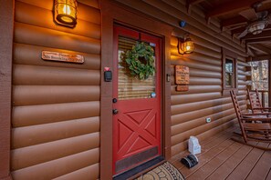 A log cabin with a red door, a 'No Smoking/No Pets' sign, a wreath, and a 'Gone to Therapy' sign. - Luxury Cabin with Mountain Views and Amenities (GATLINBURG)