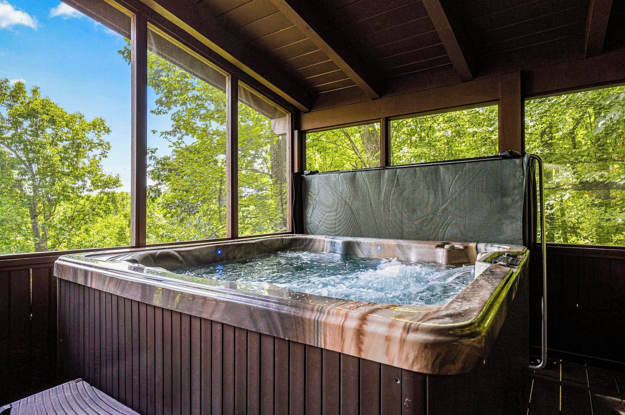 A hot tub with a wooden exterior, large windows, and a view of trees.