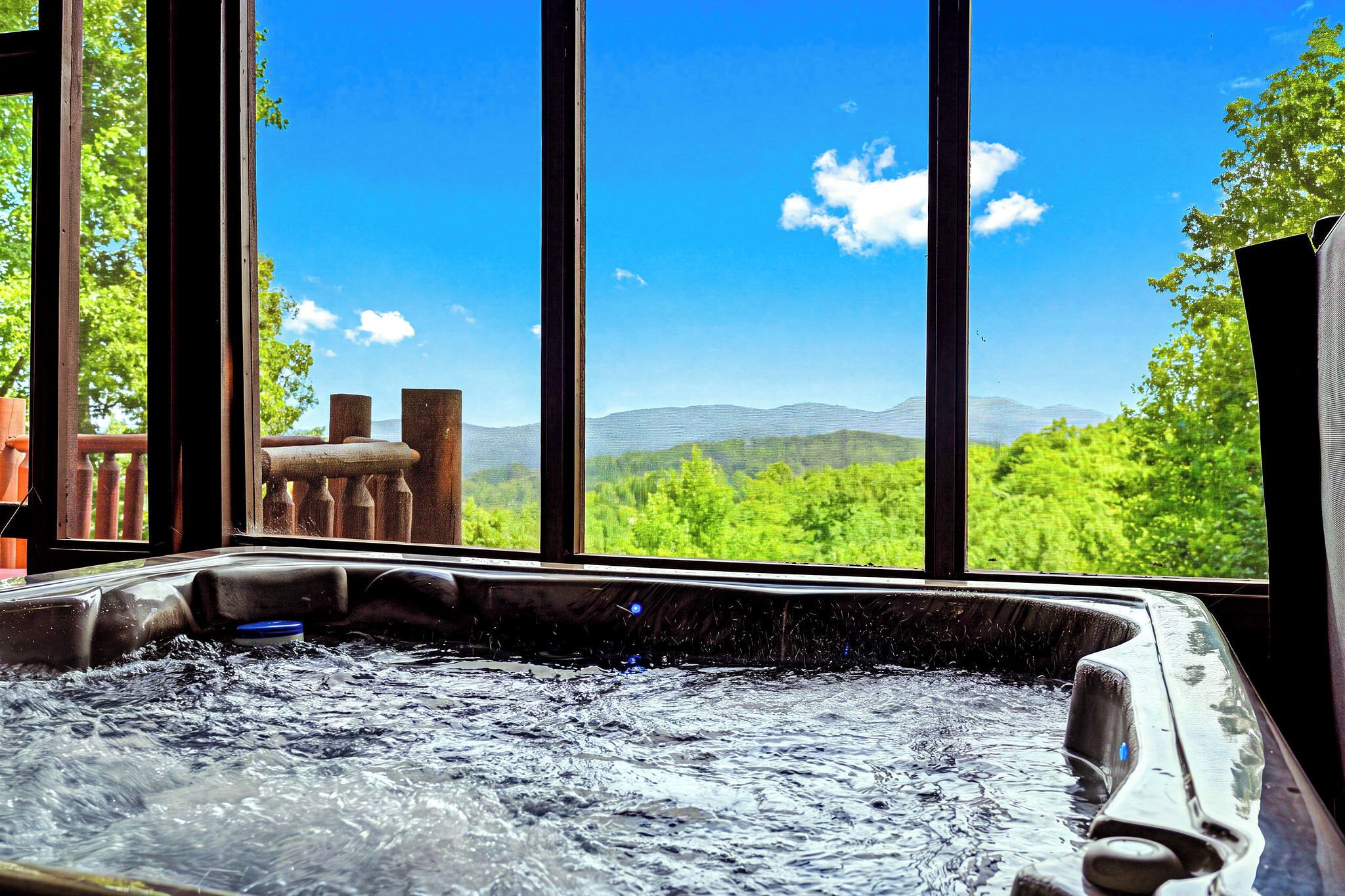 A hot tub with a view of green hills and mountains through large windows.