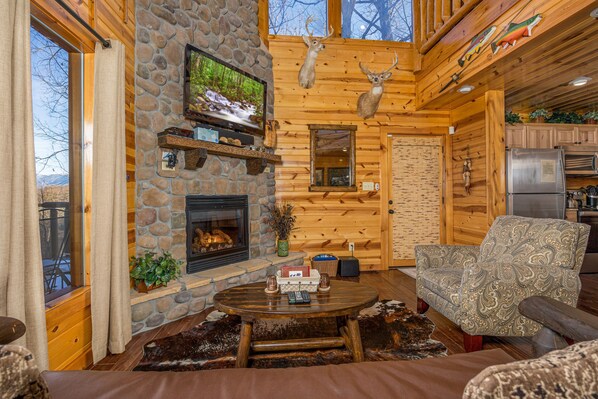 Ein Blockhaus-Interieur mit Kamin aus Stein, einem Fernseher, aufgehängten Hirschgeweihen und einer Küchenzeile.