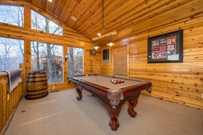 Un interior de madera con mesa de billar, ventanas y un mapa enmarcado en la pared.