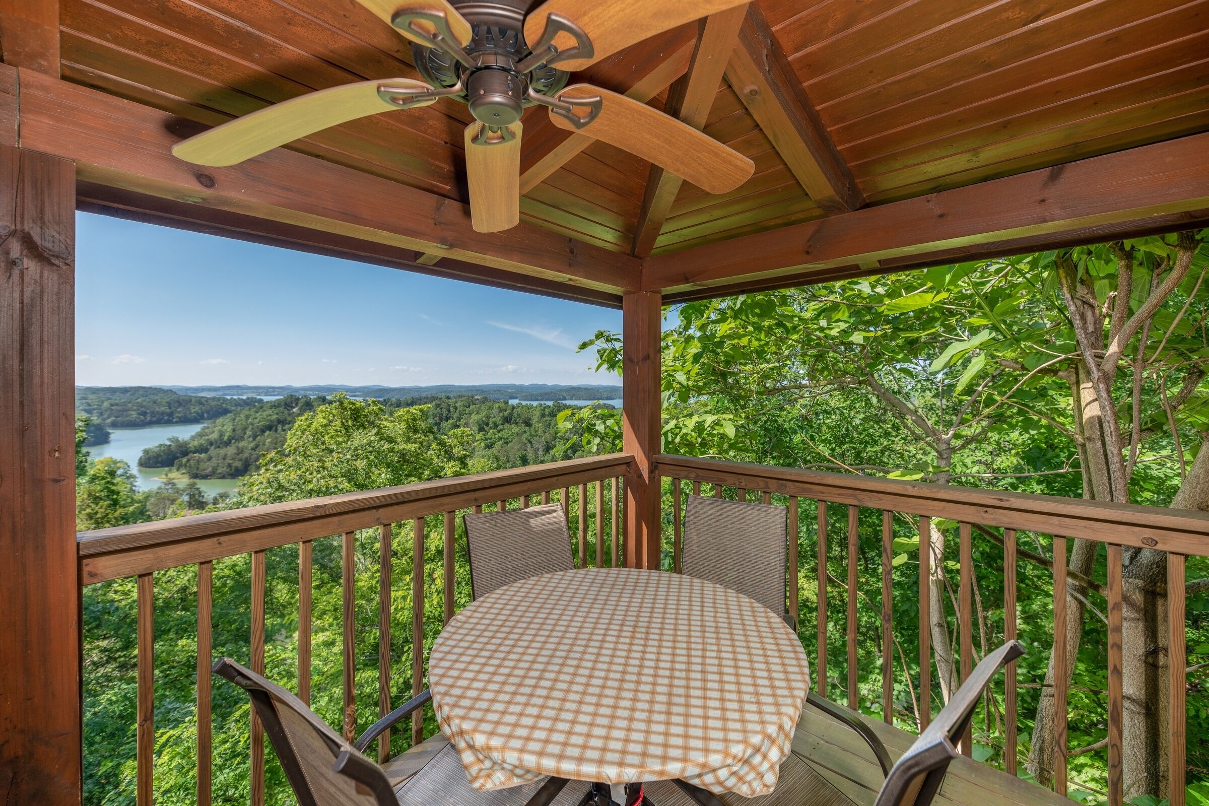 Une terrasse en bois avec une table et des chaises, offrant une vue sur un paysage luxuriant comprenant un lac et une forêt.