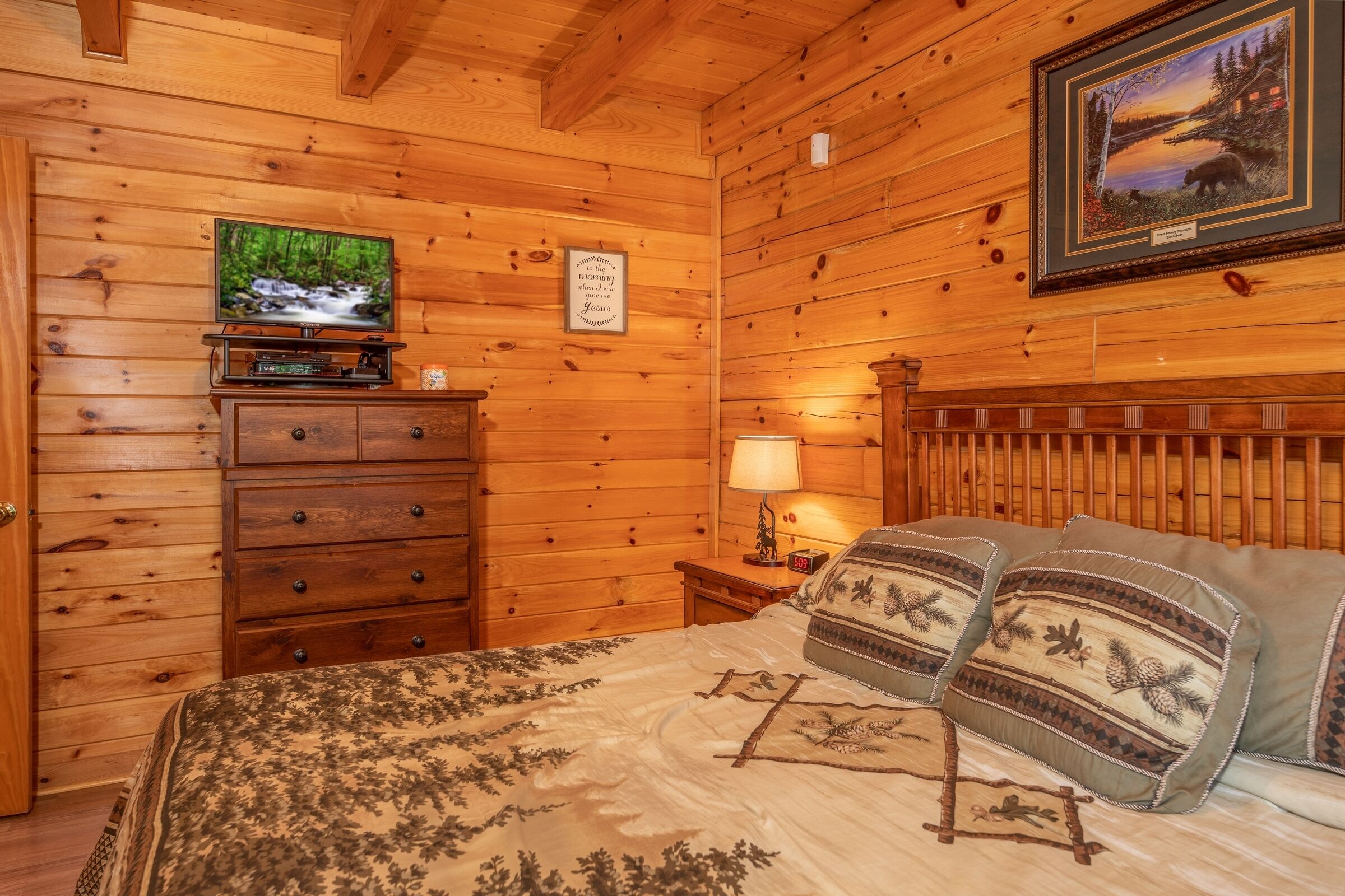Une pièce de style cabane en bois, avec un lit, une commode, une télévision et un tableau encadré au mur.