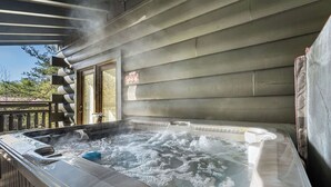 A hot tub with steam rising, surrounded by wooden deck and a building with large windows.