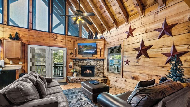 A cozy cabin interior with a stone fireplace, leather sofas, and wooden walls.