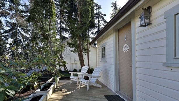 A wooden deck with white Adirondack chairs, a small table, and a lantern.