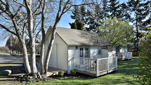 A small, single-story house with a porch, surrounded by trees and a well-maintained lawn.