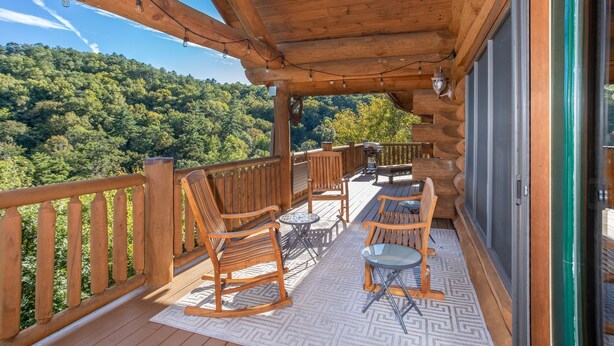 A wooden deck with outdoor furniture, a patterned rug, and a scenic forest view. - Luxury Log Lodge with Mountain Views (SEVIERVILLE)