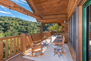 A wooden deck with outdoor furniture, a patterned rug, and a scenic forest view. - Luxury Log Lodge with Mountain Views (SEVIERVILLE)