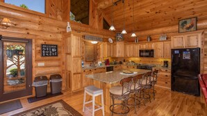 A wooden cabin interior with a kitchen featuring a central island, bar stools, a refrigerator, and a dining table. - Luxury Log Lodge with Mountain Views (SEVIERVILLE)