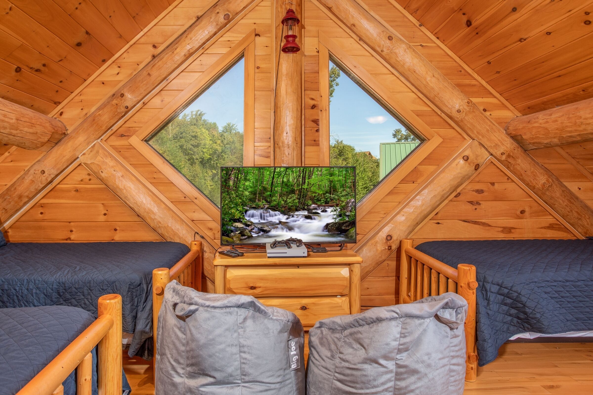 Un dormitorio acogedor en el ático con un televisor sobre una mesa de madera, dos camas y un ventanal grande.