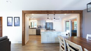 A modern kitchen with white cabinets, a central island, and a dining area with a wooden table and chairs. - Dollar Lake Oasis, Near Downtown and the Chain, Fire Pit, Sandy Beach, W&D, WiFi (Eagle River)