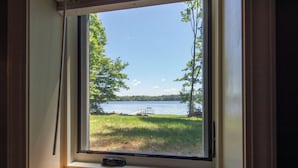 A window with a view of a lake, surrounded by trees and a dock. - Dollar Lake Oasis, Near Downtown and the Chain, Fire Pit, Sandy Beach, W&D, WiFi (Eagle River)