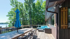 A wooden deck with a table and chairs, a blue umbrella, and a sofa with blue cushions. - Dollar Lake Oasis, Near Downtown and the Chain, Fire Pit, Sandy Beach, W&D, WiFi (Eagle River)
