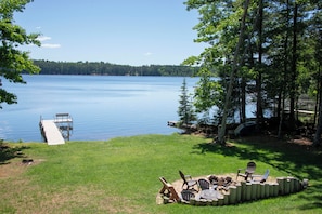 A lakeside deck with a dock, outdoor seating, and a fire pit.