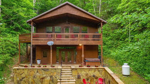 A two-story wooden cabin with a balcony, stone steps, and outdoor seating. - Private Cabin with Game Room (SEVIERVILLE)