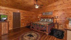 A log cabin bedroom with a bed, a ceiling fan, a television, and a wooden door. - Private Cabin with Game Room (SEVIERVILLE)