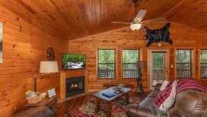 A cozy cabin interior with wooden walls, a fireplace, leather sofas, and a ceiling fan. - Private Cabin with Game Room (SEVIERVILLE)