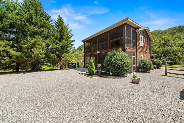 A two-story wooden house with a gravel driveway and a fenced yard. - Heaven Sent - Tastefully Decorated Cabin with Fireplace (PIGEON FORGE)