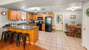 Una cocina con armarios de madera, un refrigerador negro, un microondas y una cafetera. Hay un comedor con una mesa y sillas.
