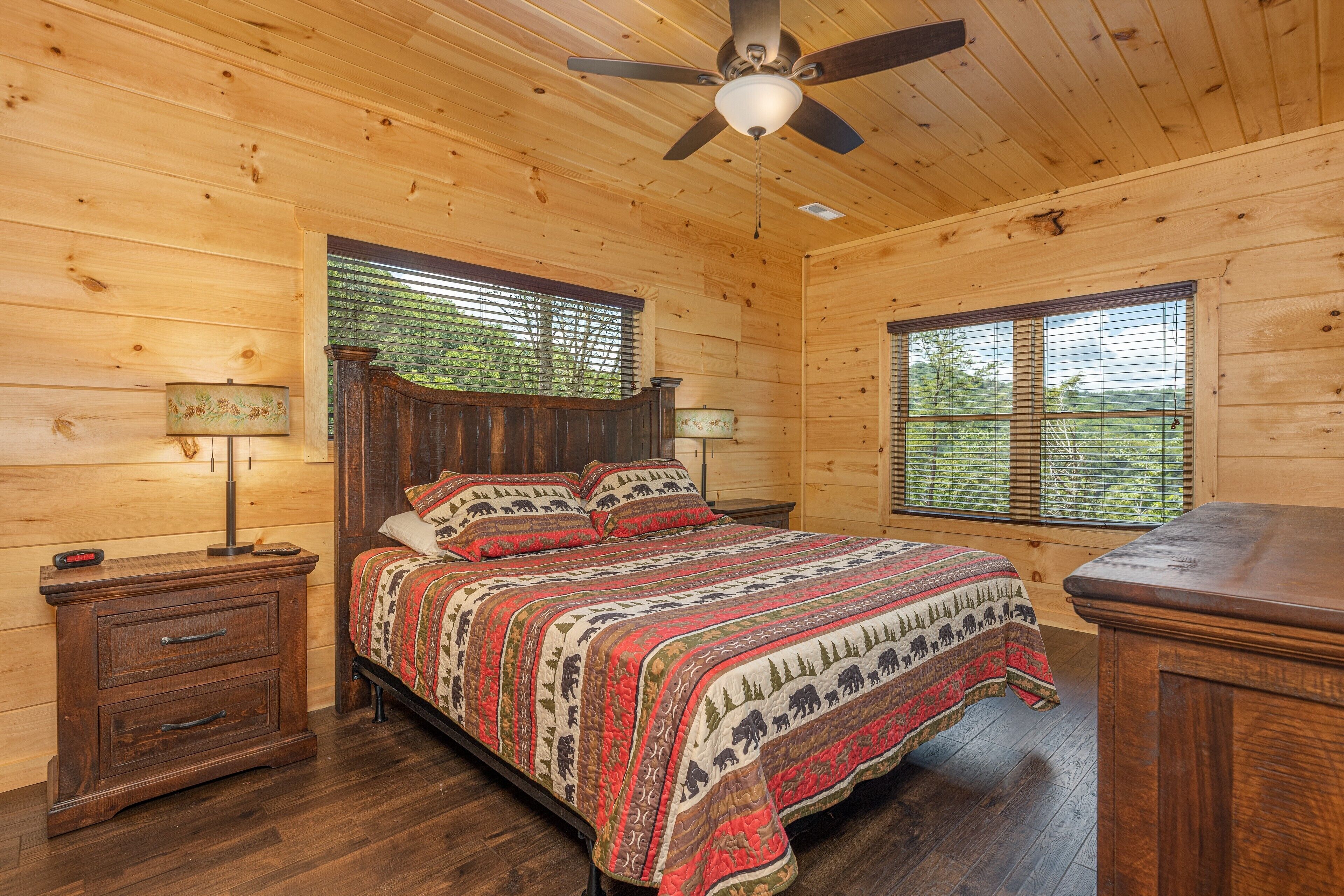 Ein Schlafzimmer einer Holzhütte mit einem Bett, Nachttischen und einem Deckenventilator.
