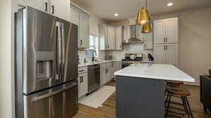 A modern kitchen with stainless steel appliances, white cabinetry, a marble island, and a bar stool. - The Wooden Sanctuary (SEVIERVILLE)