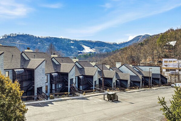 A row of modern buildings with external staircases, a parking lot, and a mountainous backdrop. - A Mountain Top Retreat (GATLINBURG)