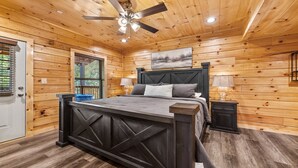 Une chambre dans une cabane en bois, avec un lit, un ventilateur de plafond et une fenêtre équipée de stores.
