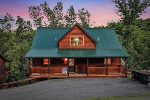 A log cabin with a green metal roof, a front porch, and a visible window. - Hillbilly Hideaway: A Modern Farmhouse! (PIGEON FORGE)