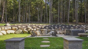 A stone patio with two benches, surrounded by a stone wall and a forest backdrop.