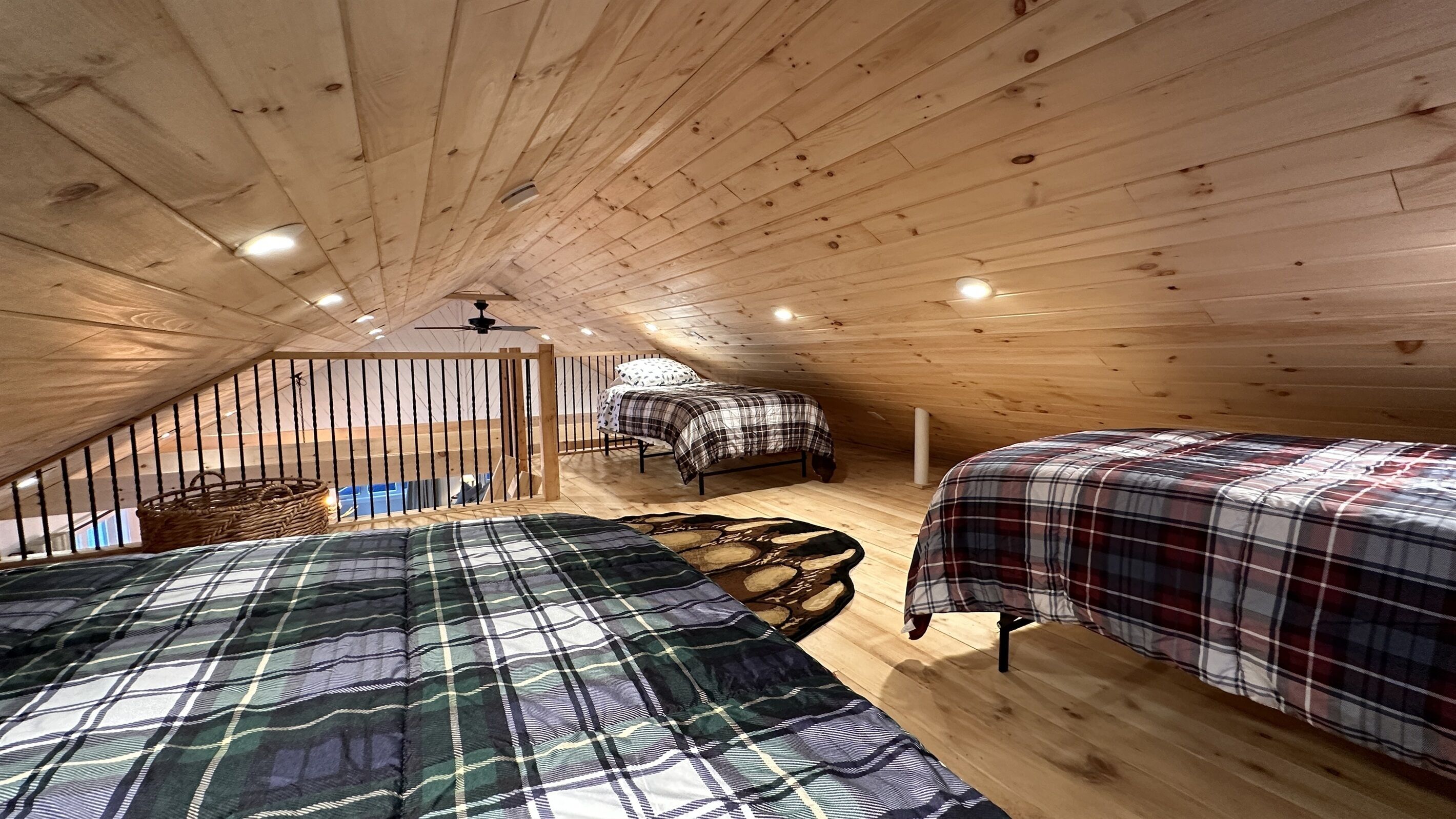 A cozy attic bedroom with wooden beams, two beds with plaid bedding, a small window, and a ceiling fan.