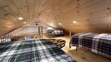 A cozy attic bedroom with wooden beams, two beds with plaid bedding, a small window, and a ceiling fan.