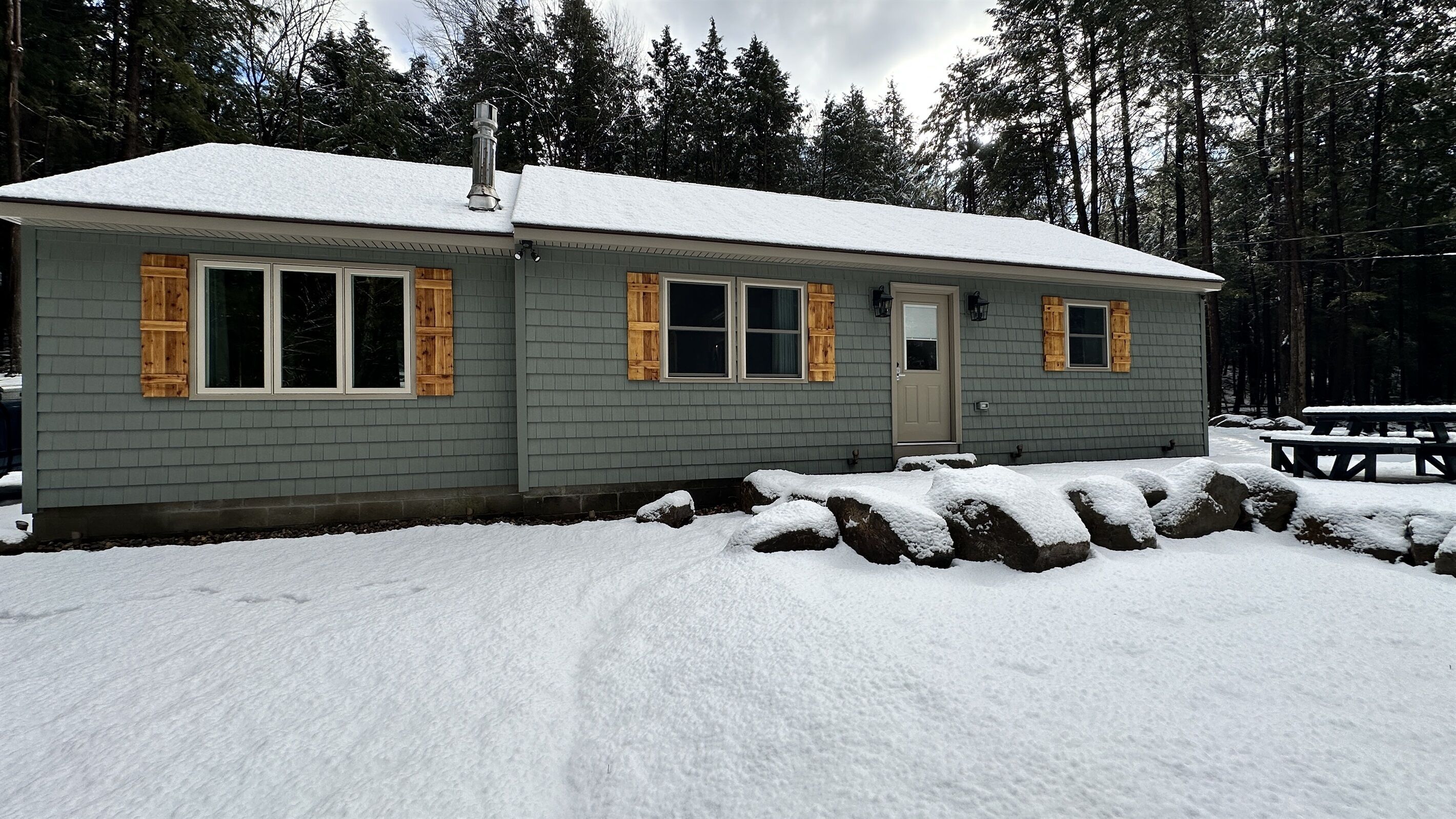 Une petite cabane dont le toit est recouvert de neige, avec des volets en bois et une cheminée.